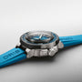 A close-up of the Oris Aquis Pro 4000M dive watch, featuring a Calibre 400 movement, blue rubber strap, black bezel with Rotation Safety System, and silver case against a light background.