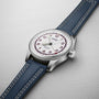 The Oris Big Crown Hank Aaron Limited Edition features a stainless steel case, white dial with red numerals, blue hour markers, and a blue leather strap with white stitching, elegantly displayed on a light gray surface.