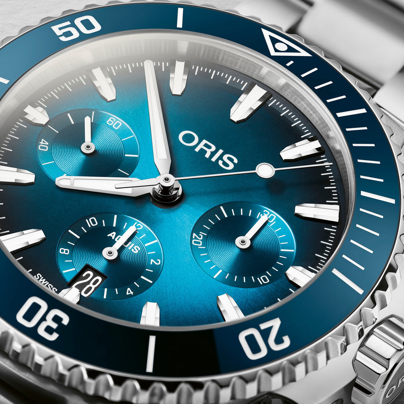 Close-up of the Oris Aquis Chronograph, featuring a blue dial with white markers, three subdials, a ceramic bezel, detailed minute and second indicators, and stainless steel construction showcasing its water resistance.