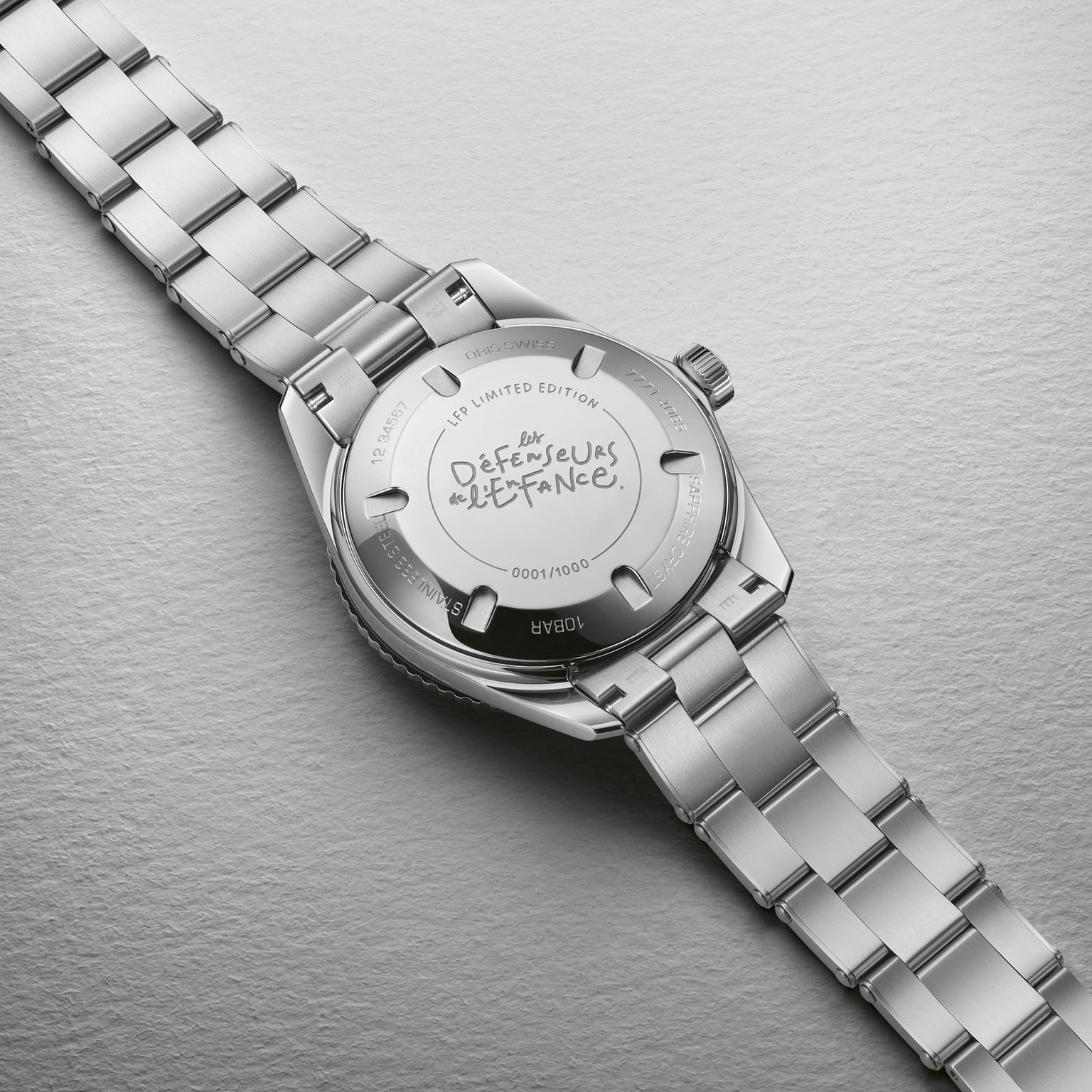 A close-up of the back of the Oris LFP Limited Edition silver wristwatch features engraved text and a handwritten “Défenseurs de l’Enfance” message, created for a charity football tournament.
