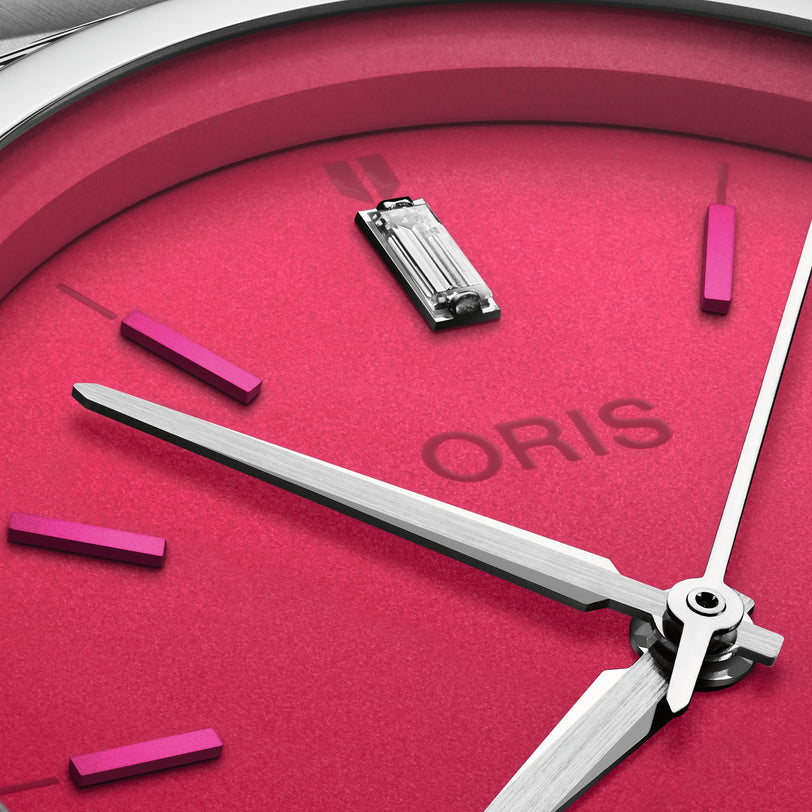 Close-up of the Oris ProPilot X Miss Piggy Edition wristwatch, showcasing a hot pink dial, silver hands, baton hour markers, and the Oris brand name.