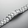 A close-up of the Oris Big Crown Pointer Date Calibre 403 stainless steel bracelet and clasp, set against a textured light grey background, showcasing its automatic movement and signature design elements.