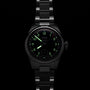 A black metal Oris Big Crown Pointer Date Calibre 403 wristwatch with luminous green numerals and hands is displayed in a dark setting, its midnight blue dial highlighting the brand’s signature automatic movement.