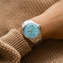 An Oris Big Crown Pointer Date Calibre 473 wristwatch with a light teal blue dial is worn on a wrist dressed in a beige knit sweater.