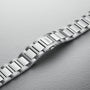 An Oris Big Crown Pointer Date stainless steel watch bracelet with a brushed and polished finish is shown diagonally on a textured light gray surface.