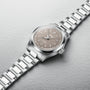 The Oris Big Crown wristwatch features a silver metal case, taupe dial, and matching metal bracelet, displayed on a light gray surface.
