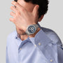 A man in a light blue shirt covers his face with his hand, displaying the Zenith Defy Skyline Skeleton - Blue watch.