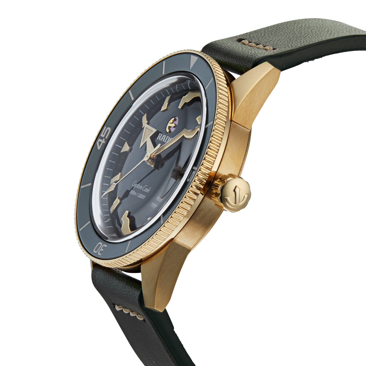 The Rado Captain Cook Automatic Bronze features a gold-tone finish with a black bezel, dark green leather strap, and visible crown, showcased at an angle against a white background.
