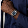 A person wearing the Rado DiaStar Original silver wristwatch with a blue face and sapphire crystal, dressed in a blue jacket over a light gray shirt.