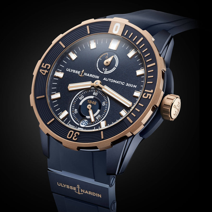 A close-up of a Ulysse Nardin Diver 44 automatic wristwatch with a blue and gold design, rotating bezel, two subdials, and advanced silicium technology, set against a dark background.