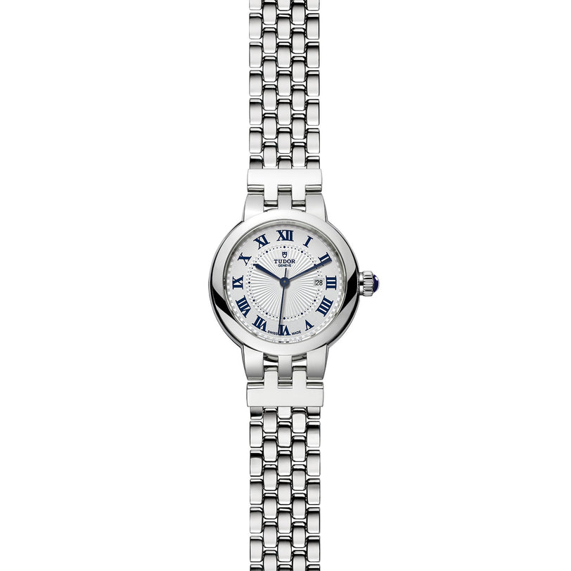 The TUDOR Clair de Rose is a silver wristwatch featuring a round face, blue Roman numerals, and a metal link band, shown on a white background.