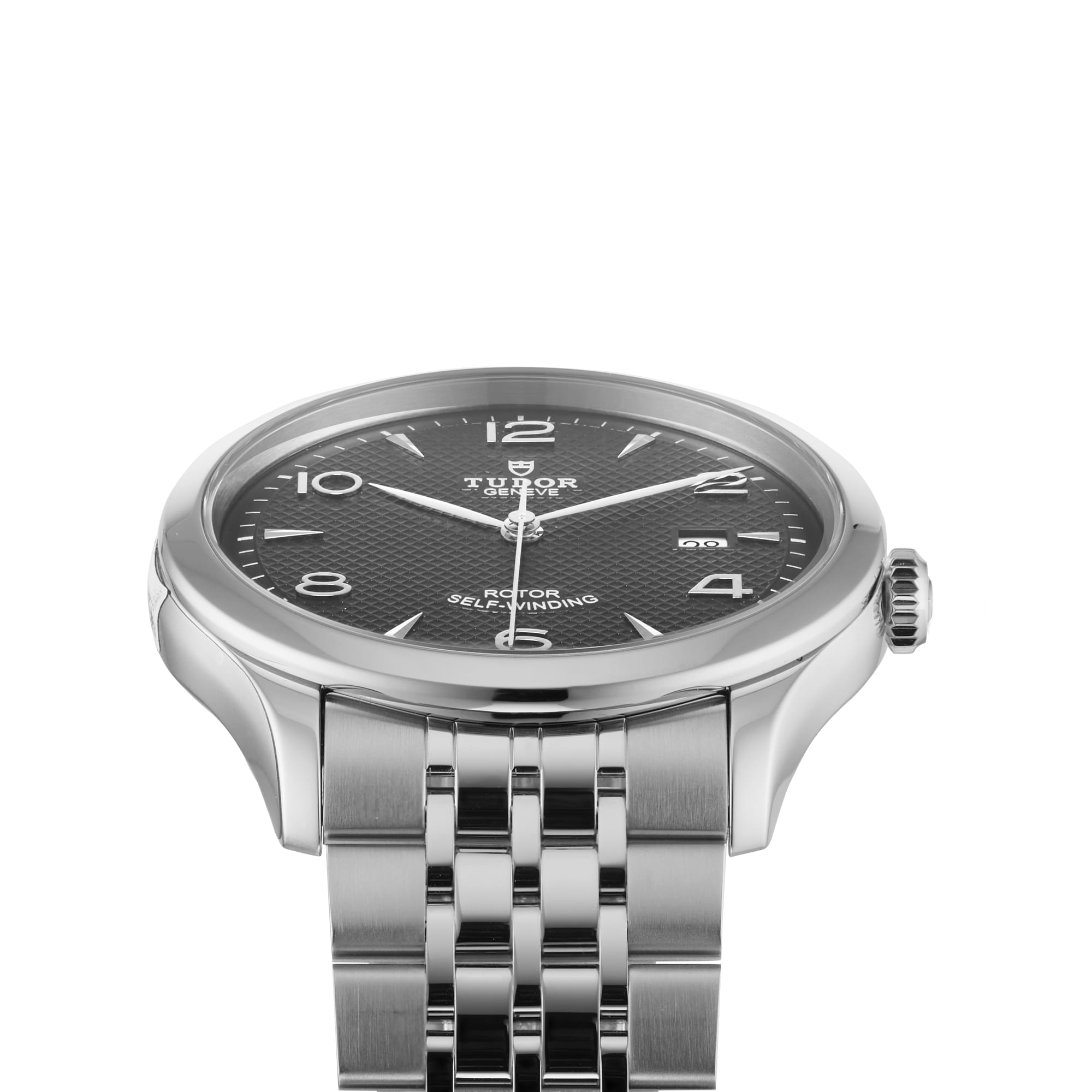 The TUDOR 1926 wristwatch features a silver case, black textured dial with silver hour markers, date at 3 o’clock, metal link bracelet, and sapphire crystal lens, shown against a white background.