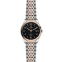 The TUDOR 1926 wristwatch features a black dial, gold-tone numerals, and a silver and rose gold bracelet, with date display at 3 o’clock.