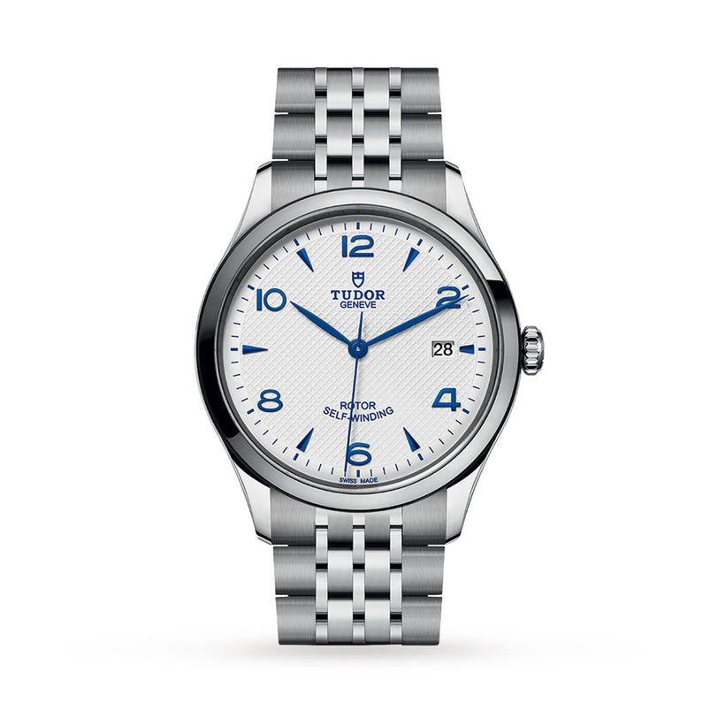 The TUDOR 1926 is a stainless steel wristwatch with a white textured dial, blue Arabic numerals and hands, a date display at 3 o’clock, and a polished silver bracelet that showcases TUDOR’s mechanical watch expertise.