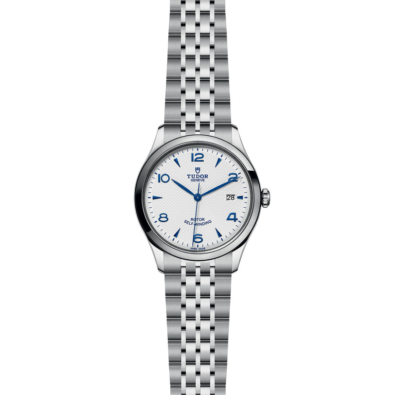 The TUDOR 1926 is a stainless steel wristwatch with a white dial, blue Arabic numerals, date display at 3 o’clock, and metal link bracelet—an elegant mechanical timepiece.