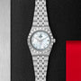 The TUDOR Royal, a stainless steel wristwatch with a mother-of-pearl dial, diamond hour markers, and date window—an automatic sport-chic timepiece—stands out on a textured black background with red and metallic highlights.