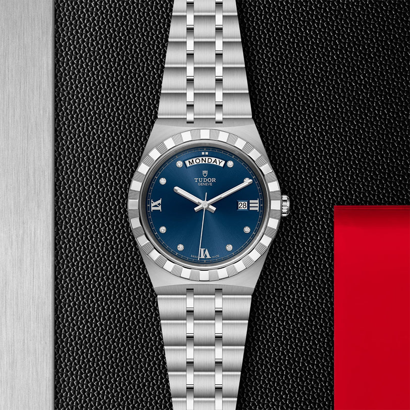 A TUDOR Royal wristwatch in silver with a blue dial, diamond markers, day-date feature, and integrated bracelet, showcased on a textured black and metallic background.