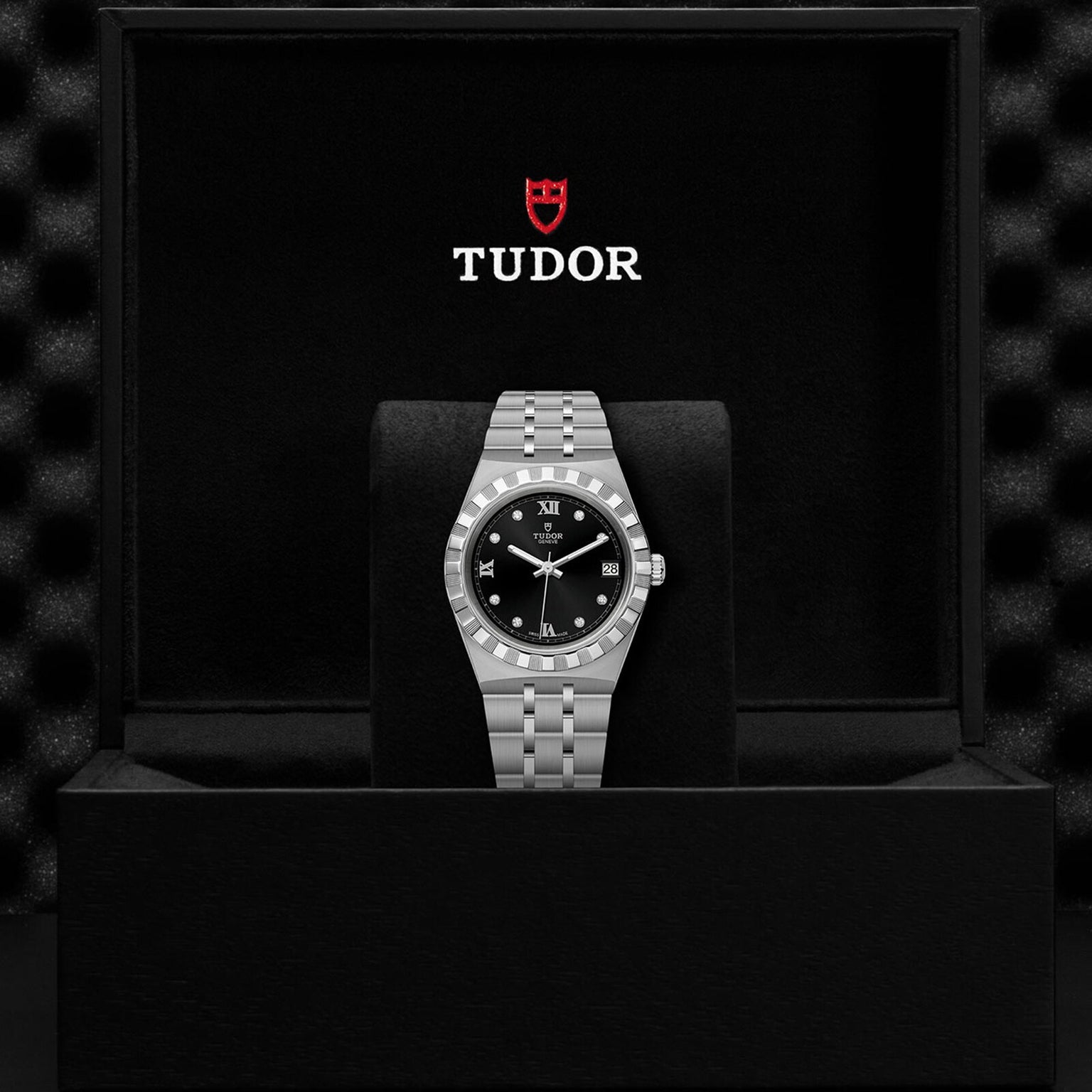 A TUDOR Royal stainless steel wristwatch with a black dial is displayed in an open TUDOR-branded box.