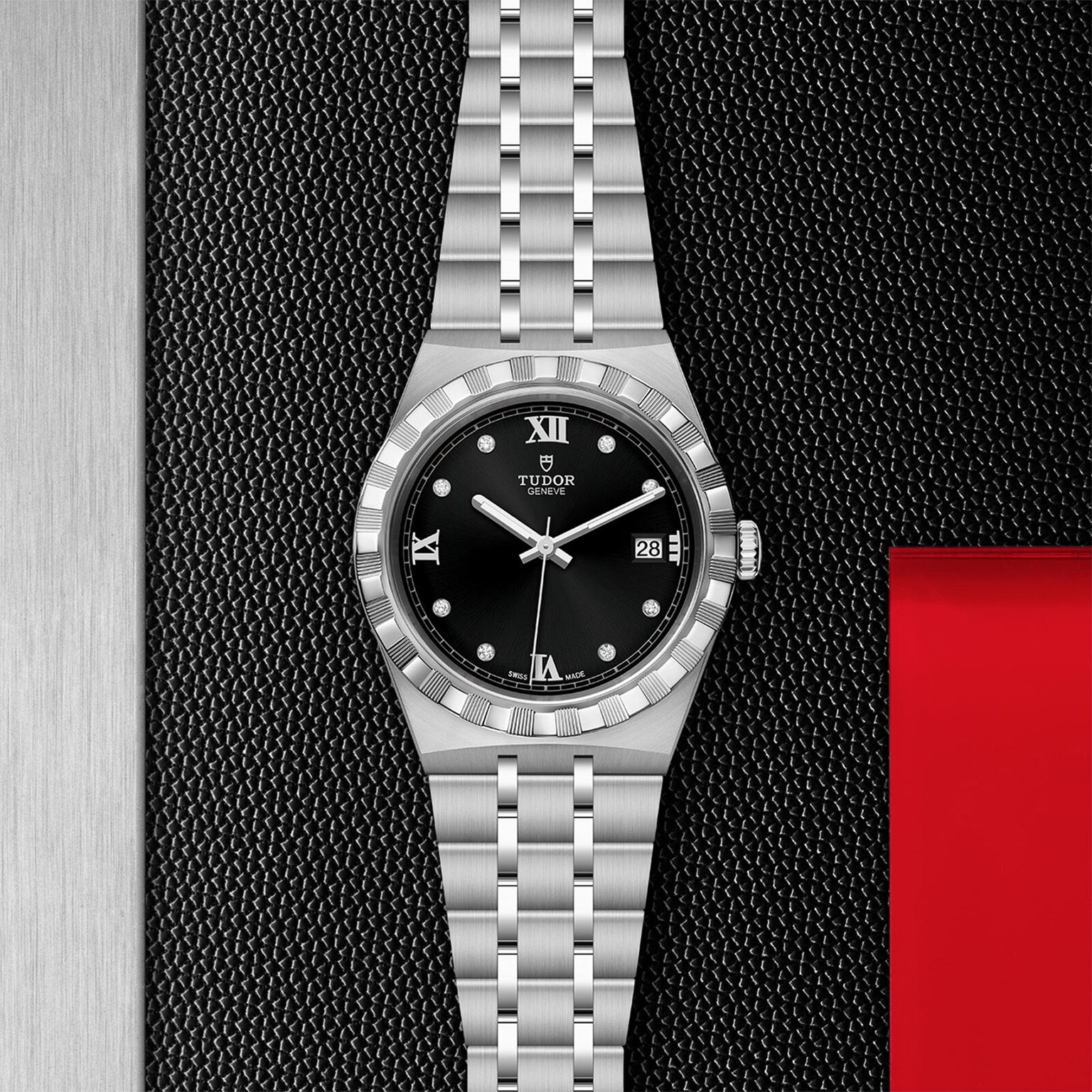 A TUDOR Royal wristwatch featuring a black dial with Roman numerals, date display, and silver bracelet is showcased on a textured black and metallic background.