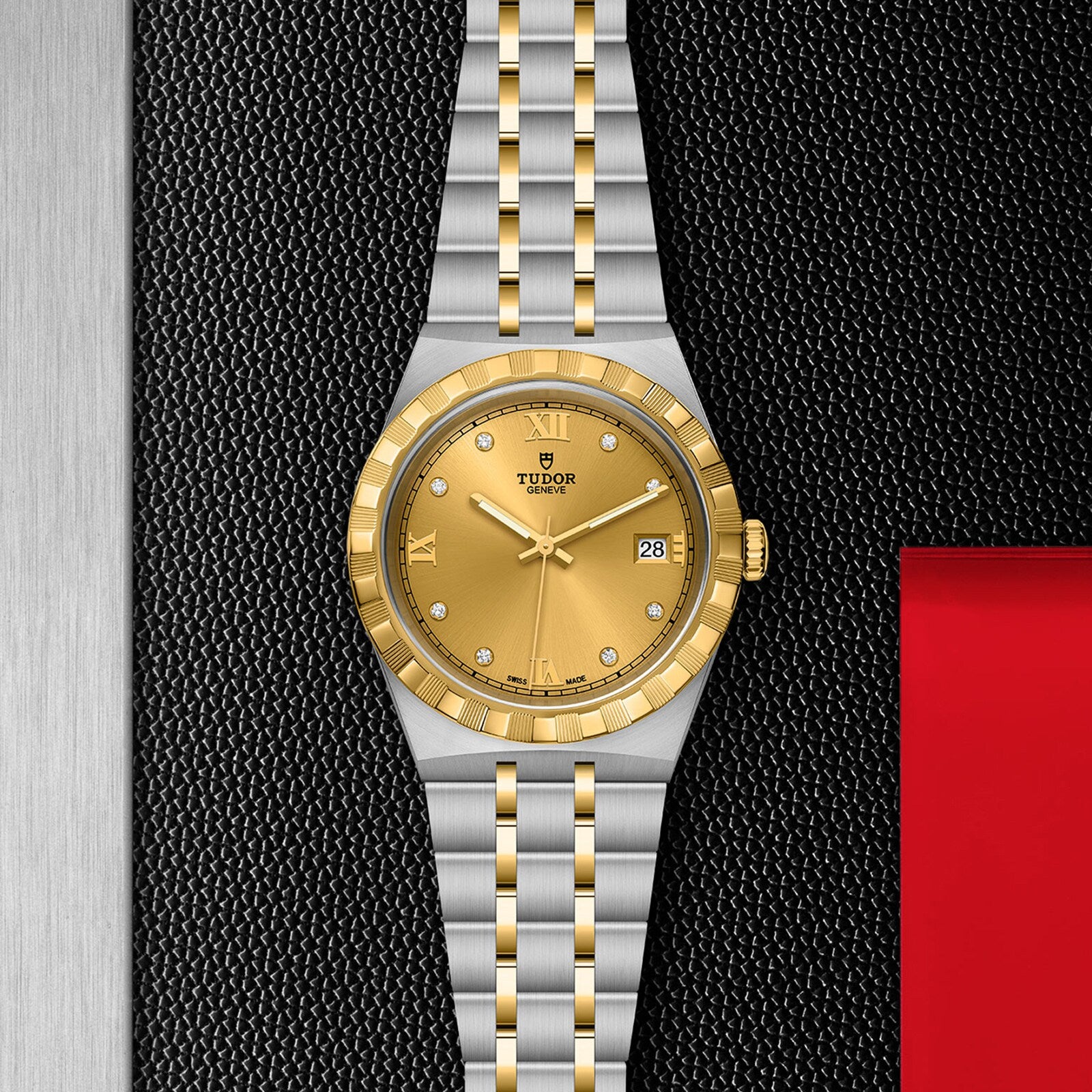 A TUDOR Royal wristwatch with a gold dial, diamond hour markers, and date display in stainless steel and gold is displayed on a textured black and red background.