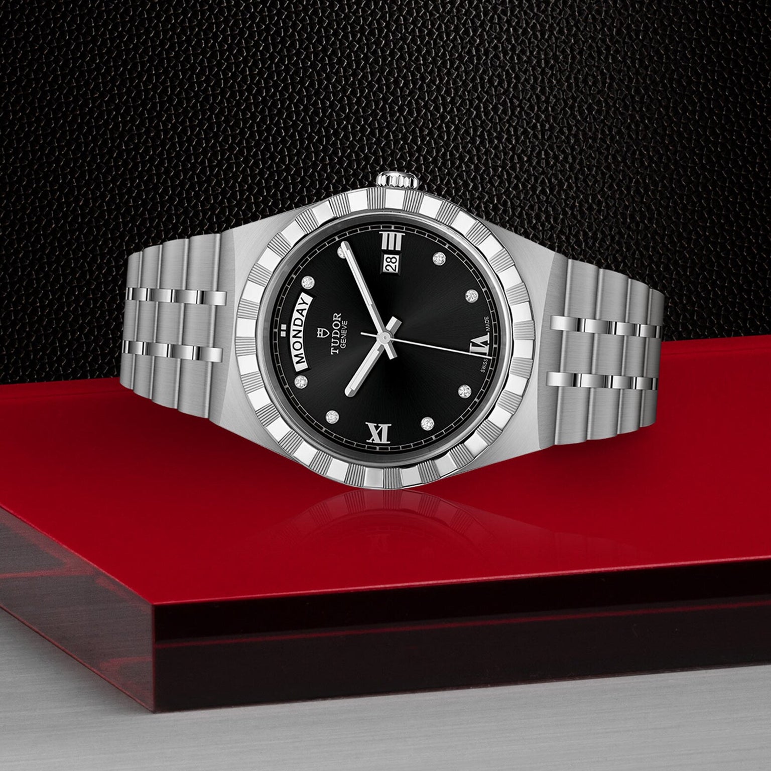 The TUDOR Royal stainless steel wristwatch features a black dial showing day, date, and time. Displayed on a red and transparent surface with a textured black background, its an elegant choice in the sport-chic watch category.