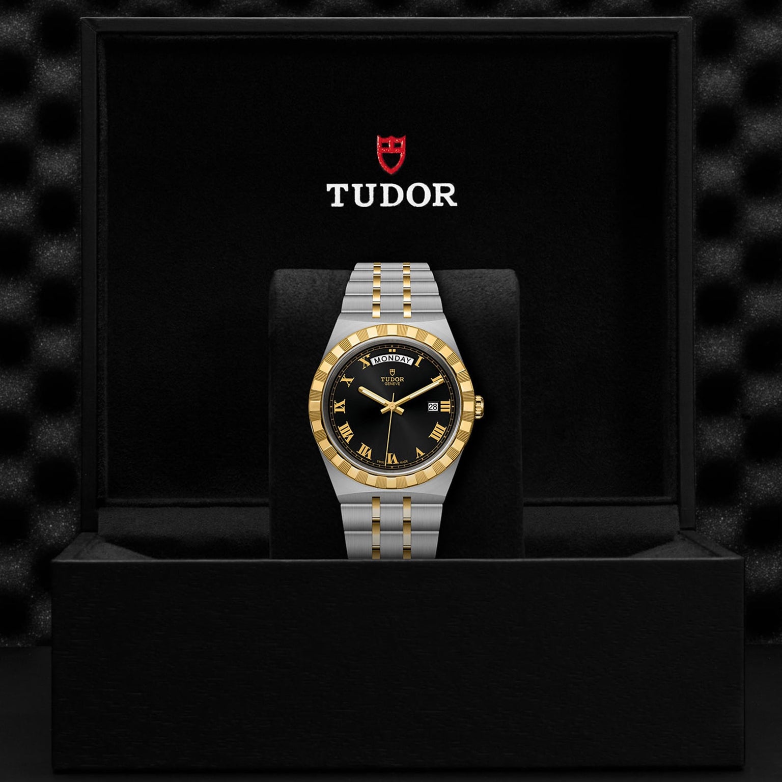 A TUDOR Royal wristwatch with a black and gold dial and integrated bracelet is displayed upright in a black Tudor presentation box, highlighting the Royal’s automatic sport-chic style.