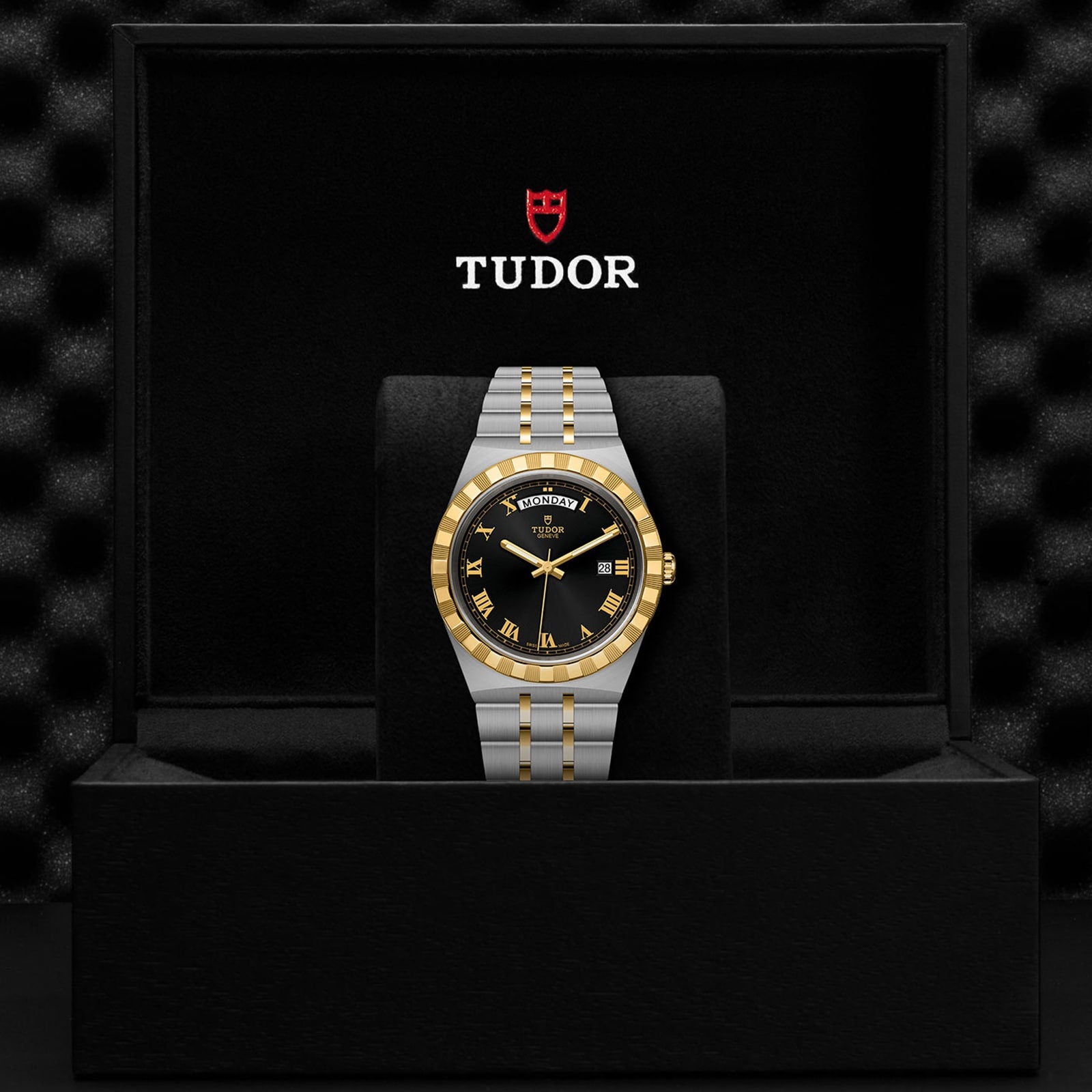A TUDOR Royal wristwatch with a black and gold dial and integrated bracelet is displayed upright in a black Tudor presentation box, highlighting the Royal’s automatic sport-chic style.
