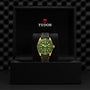 A TUDOR Black Bay 58 18K wristwatch with a green dial, gold bezel, and black strap is displayed upright in an open black box showing the TUDOR logo and crest on the inside lid.