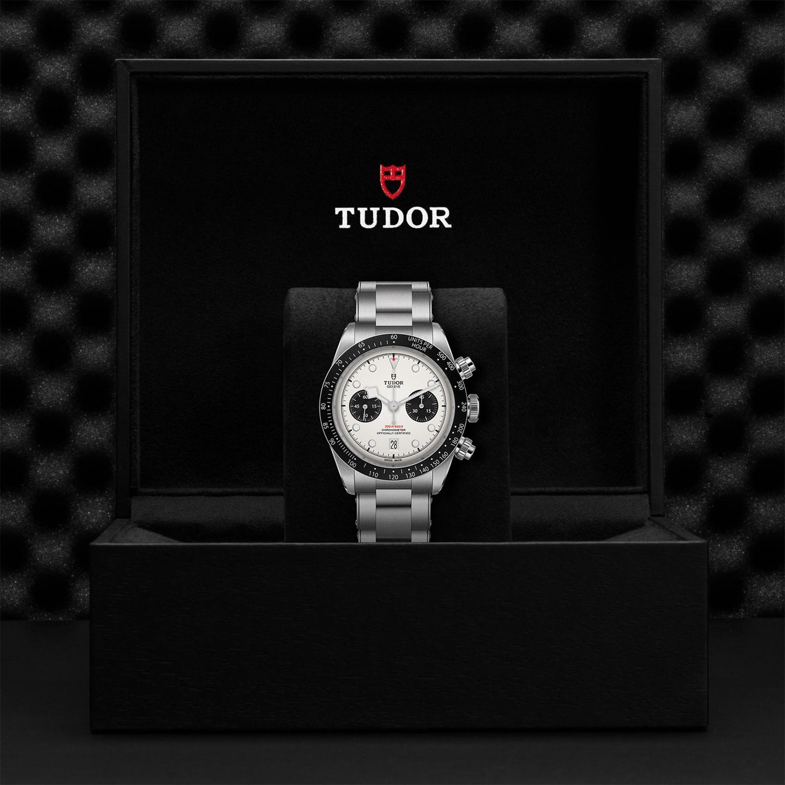 The TUDOR Black Bay Chrono wristwatch with a silver band is displayed in a black TUDOR box featuring the brand’s logo.