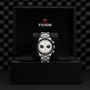 The TUDOR Black Bay Chrono wristwatch with a silver band is displayed in a black TUDOR box featuring the brand’s logo.