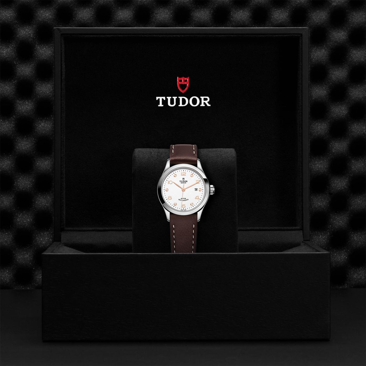 The TUDOR 1926 wristwatch features a white dial and brown leather strap, elegantly presented in a black box with the TUDOR logo—an ideal choice for admirers of classic timepieces.