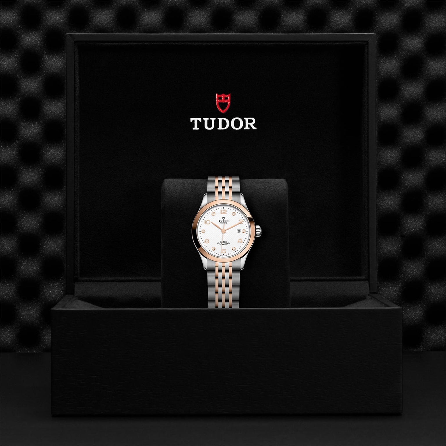 An elegant timepiece, the TUDOR 1926 wristwatch with a two-tone bracelet and white dial is showcased upright in an open black TUDOR box.