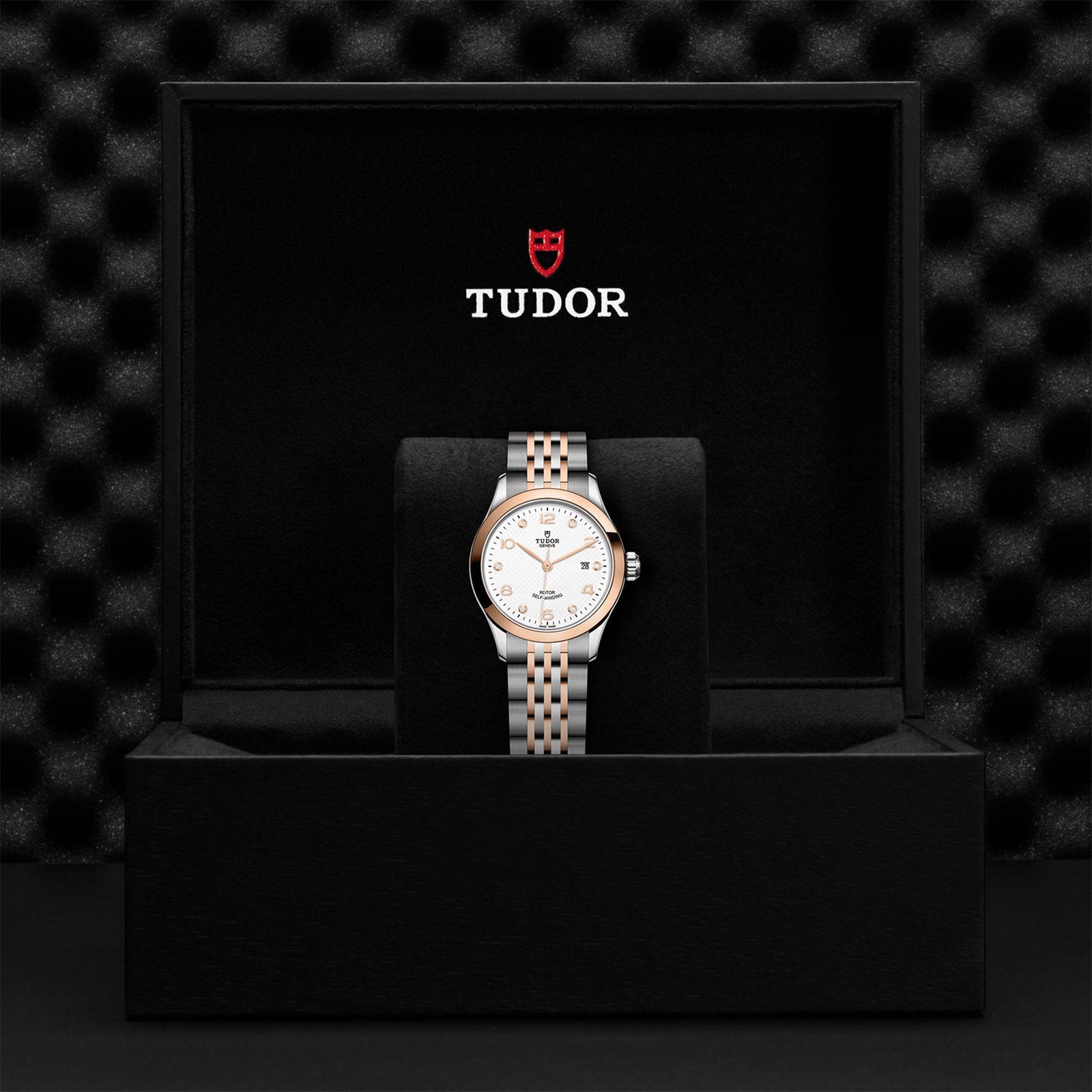An elegant timepiece, the TUDOR 1926 wristwatch with a two-tone bracelet and white dial is showcased upright in an open black TUDOR box.