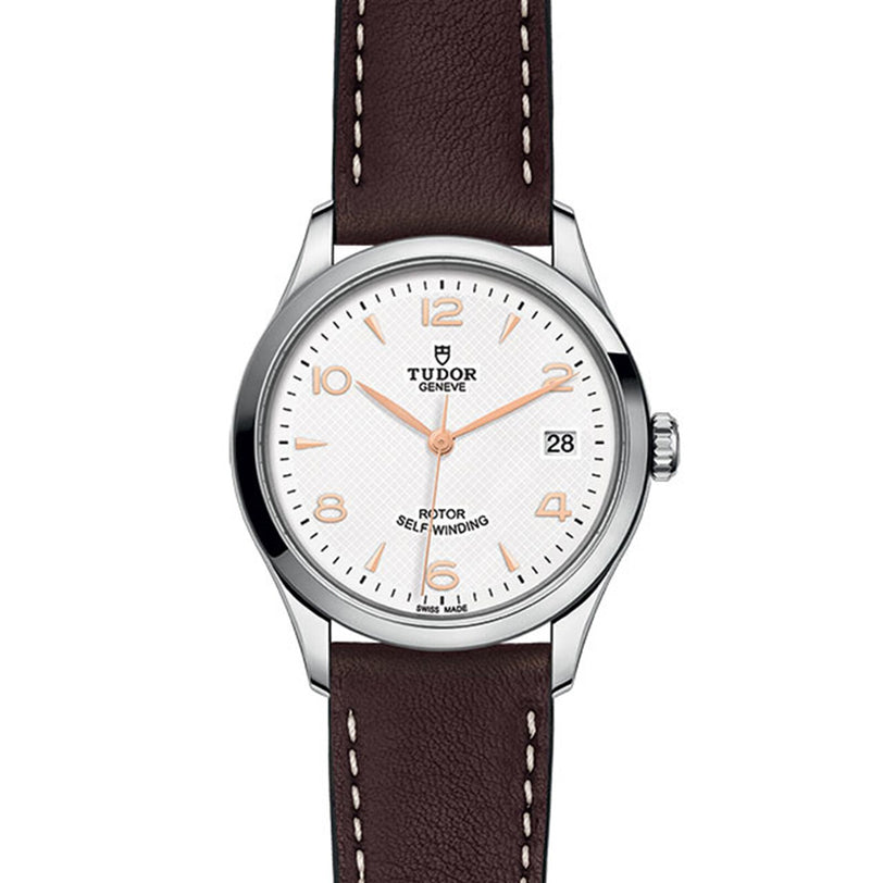 The TUDOR 1926 wristwatch features a white dial, brown leather strap, and date display at 3 o’clock.