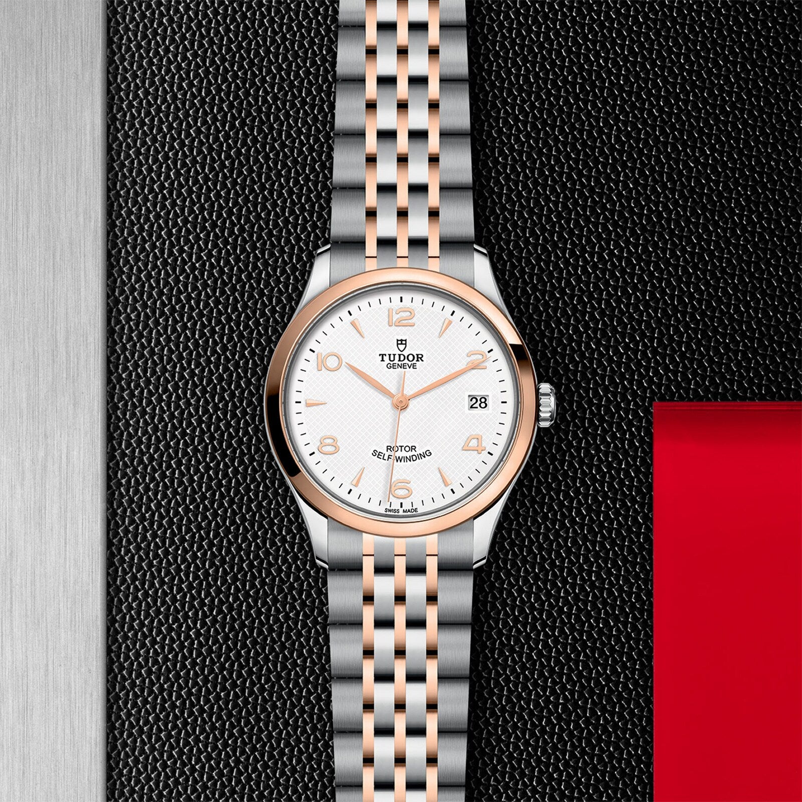 A TUDOR 1926 wristwatch with a silver and rose gold band displayed on a textured black surface.