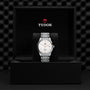 The TUDOR 1926 wristwatch, featuring a silver metal band and white dial, is showcased upright in an open black box with TUDOR branding.