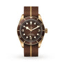 The TUDOR Black Bay 58 Bronze is a Swiss-made watch with a brown dial, bronze case, gold-tone accents, and a brown fabric strap featuring a gold stripe. It displays hours, minutes, and seconds.
