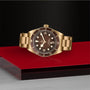 The TUDOR Black Bay 58 Bronze wristwatch with a brown dial is displayed on a glossy red and black platform.