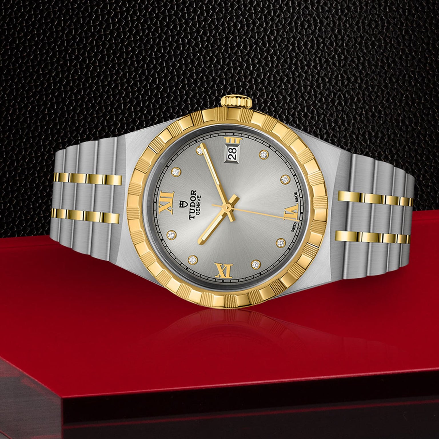 A TUDOR Royal wristwatch featuring a gold bezel, silver dial with Roman numerals, date display, and integrated bracelet is showcased against a red and black background.