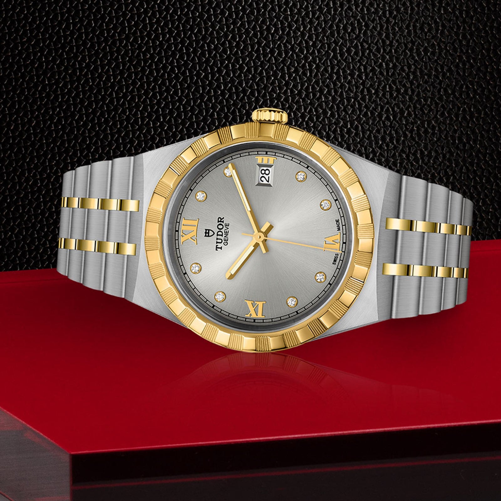 A TUDOR Royal wristwatch featuring a gold bezel, silver dial with Roman numerals, date display, and integrated bracelet is showcased against a red and black background.