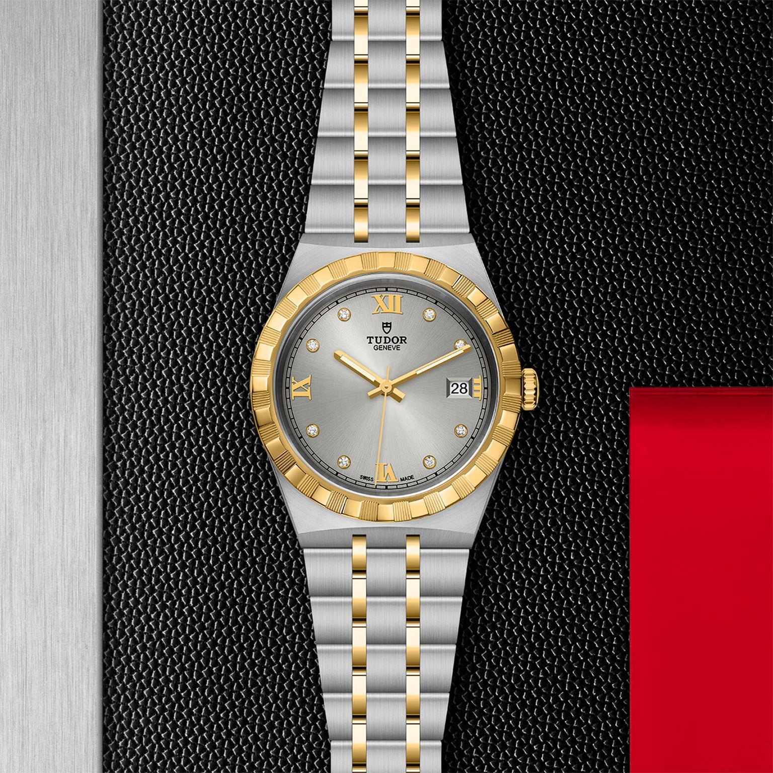 A TUDOR Royal wristwatch in silver and gold, featuring a grey dial with date display, displayed on a textured black surface.