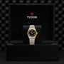 A TUDOR Royal wristwatch, featuring a stainless steel and gold two-tone band with a black-and-gold bezel, is presented in an open Tudor-branded black box, exemplifying the refined sport-chic style of automatic watches.