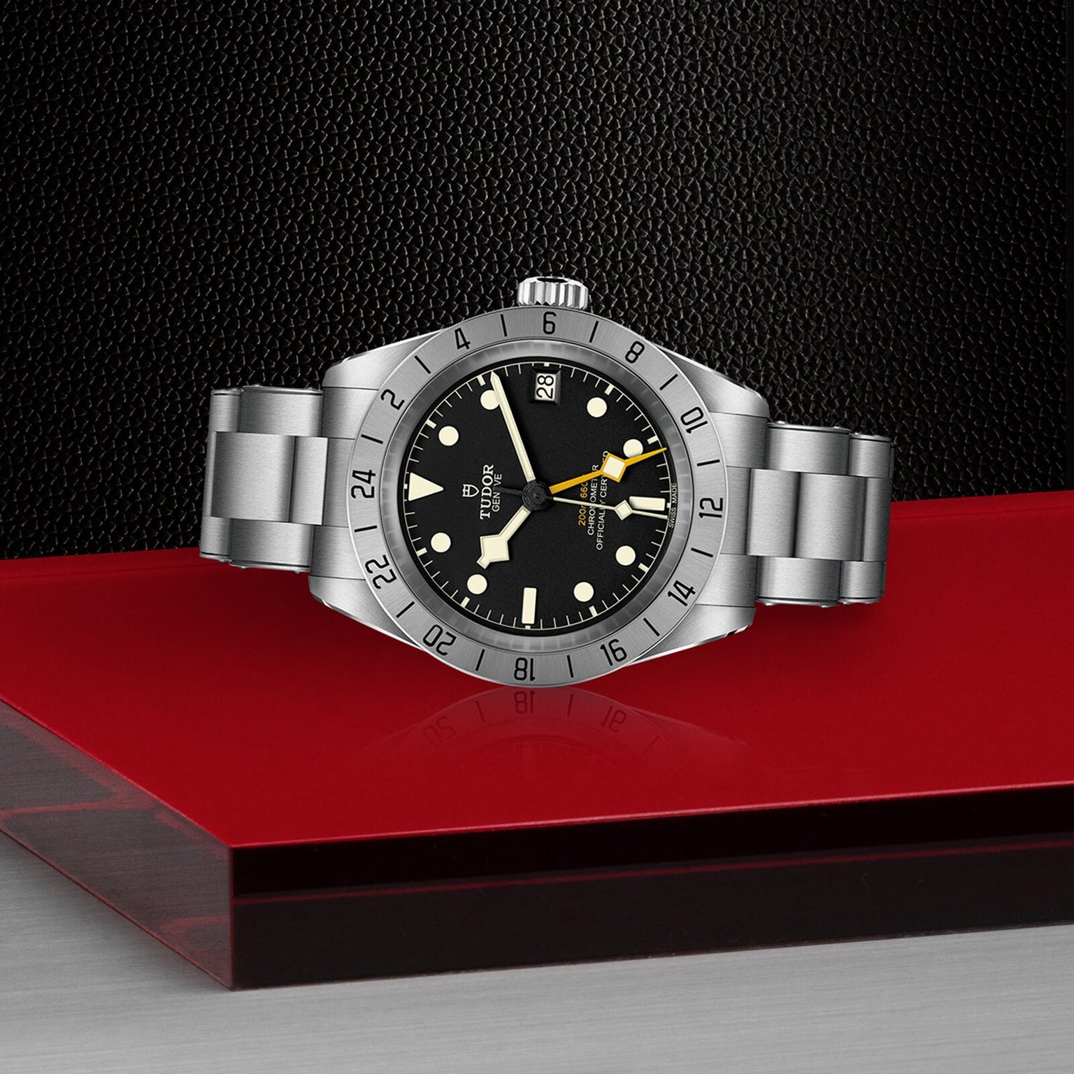 A TUDOR Black Bay Pro stainless steel wristwatch with a black dial and silver bezel is displayed on glossy red and matte black surfaces, capturing the modern essence of TUDOR’s acclaimed divers’ watches.