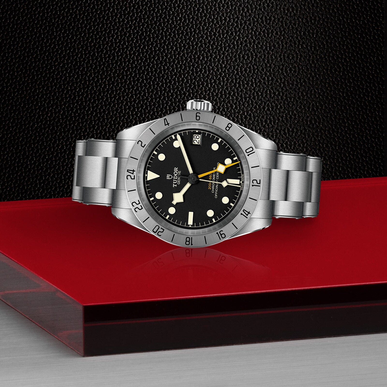 A TUDOR Black Bay Pro stainless steel wristwatch with a black dial and silver bezel is displayed on glossy red and matte black surfaces, capturing the modern essence of TUDOR’s acclaimed divers’ watches.