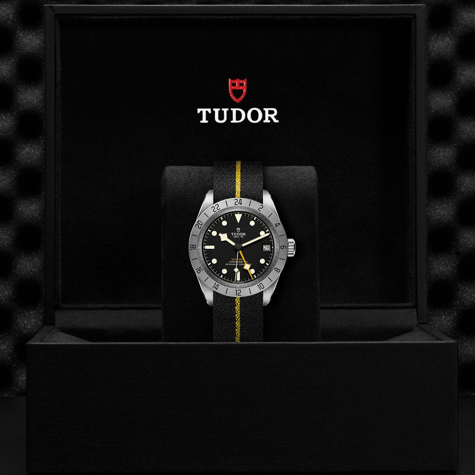 A neo-vintage TUDOR Black Bay Pro wristwatch with a black and yellow strap is displayed in an open black box featuring the TUDOR logo inside, reflecting the enduring legacy of TUDOR divers’ watches.