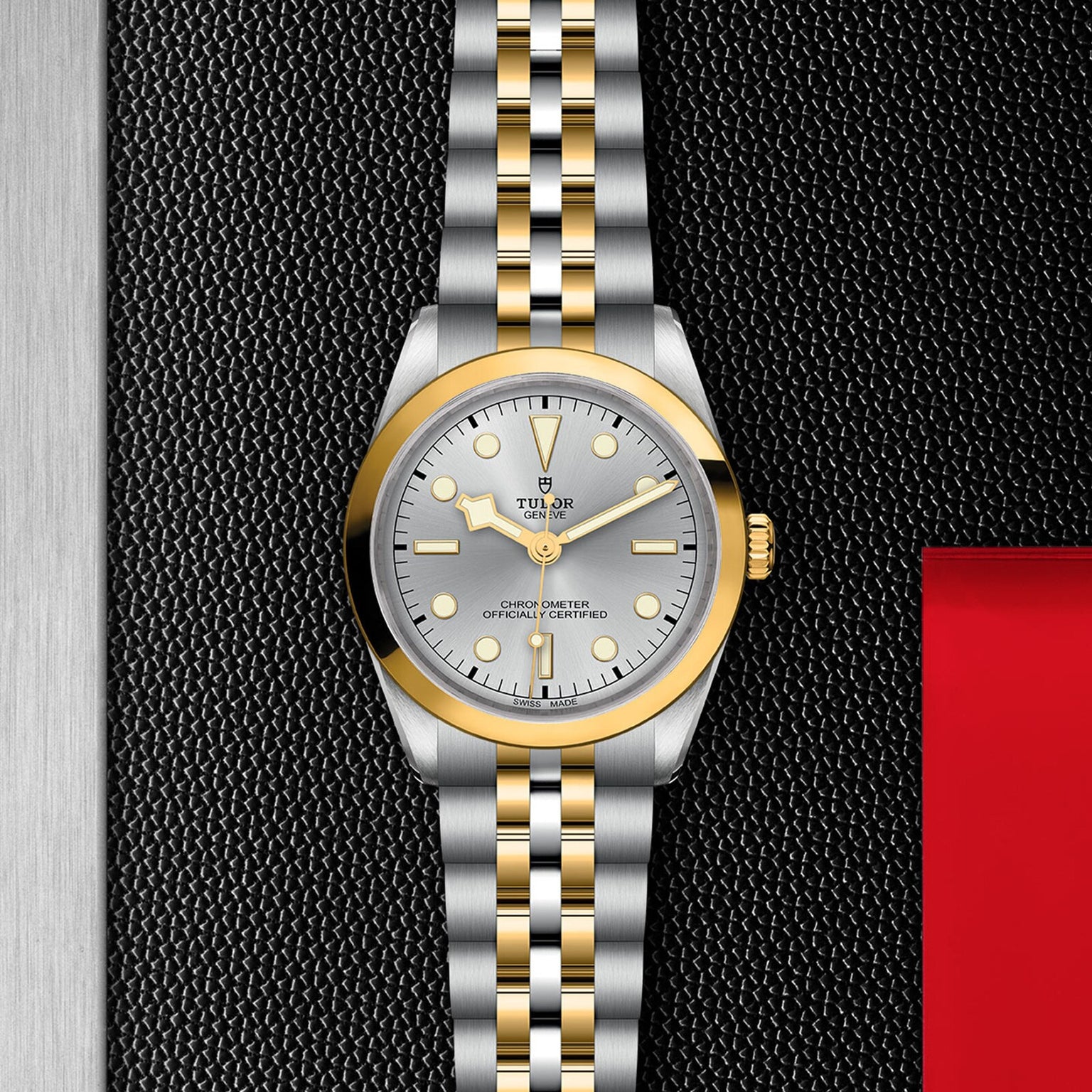 The TUDOR Black Bay One 36 S&G features a silver and gold two-tone bracelet, silver dial, gold bezel, and markers, shown on a textured black background.