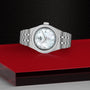 A TUDOR Royal wristwatch with a white mother-of-pearl dial is displayed on a red and black surface.