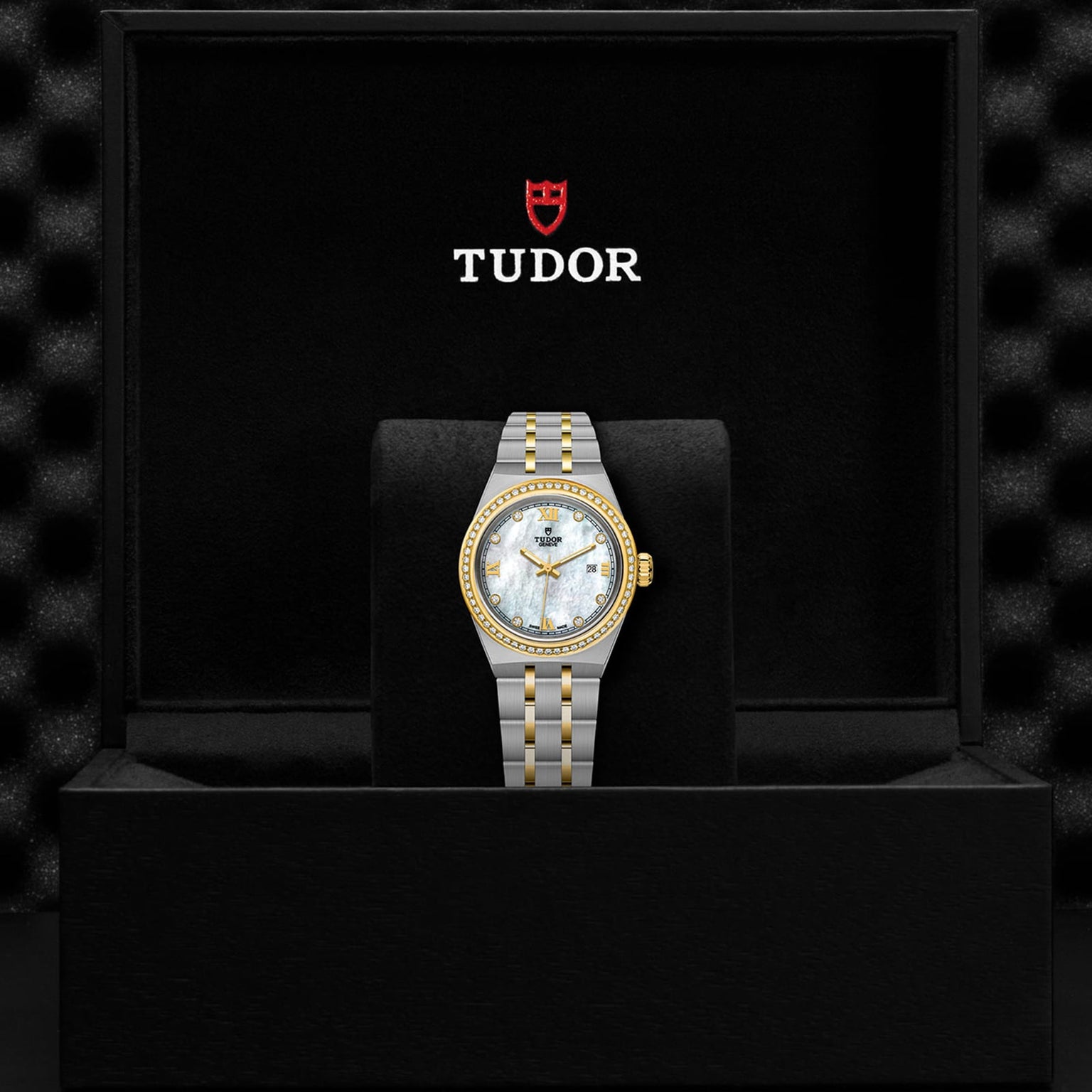 A TUDOR Royal wristwatch with a two-tone metal band, mother-of-pearl dial, and gold bezel is displayed in an open black TUDOR-branded box, highlighting the refined elegance of the Royal line.