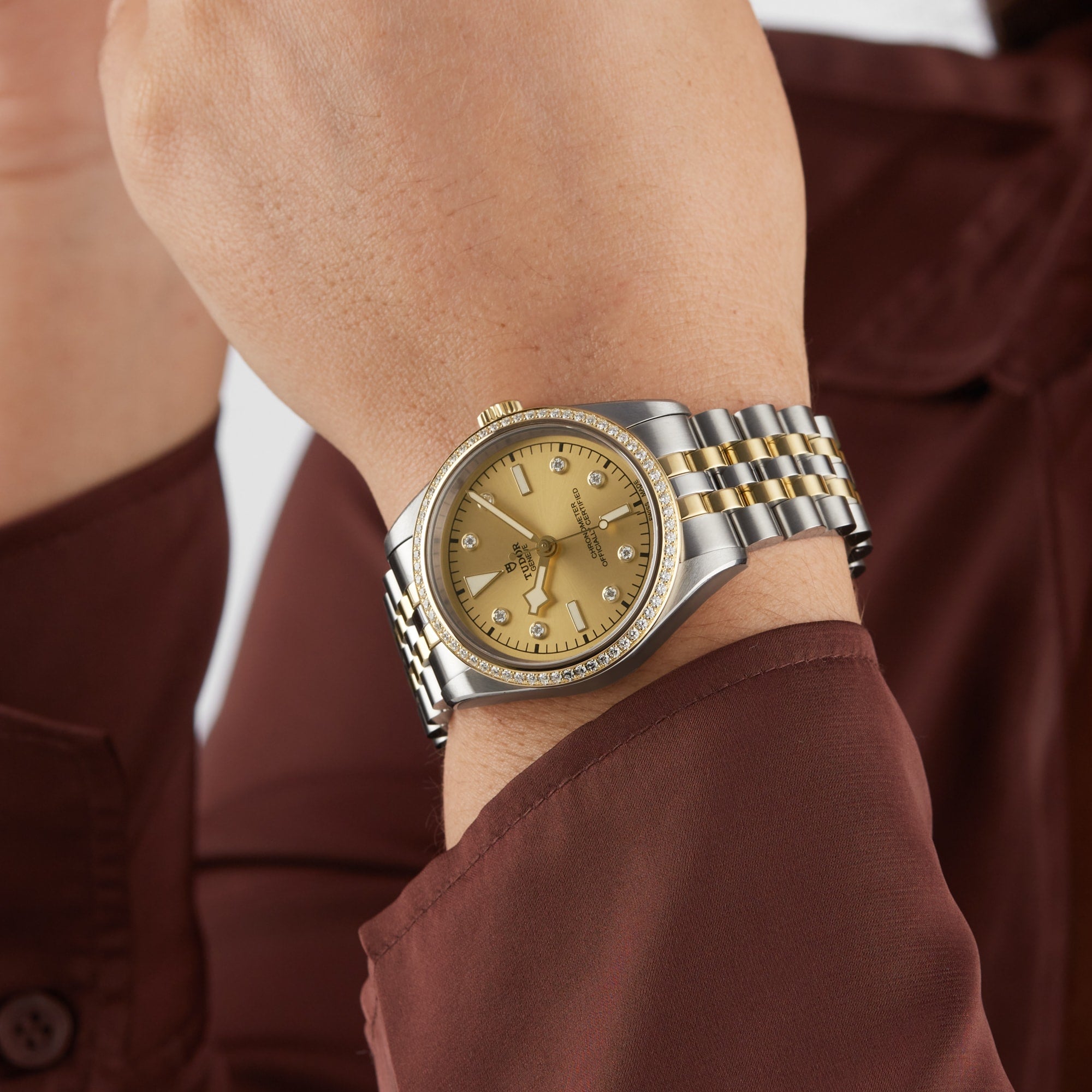 A close-up of a persons wrist wearing a TUDOR Black Bay One 36 S&G wristwatch, featuring a gold dial and diamond hour markers.