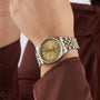 A close-up of a persons wrist wearing a TUDOR Black Bay One 36 S&G wristwatch, featuring a gold dial and diamond hour markers.